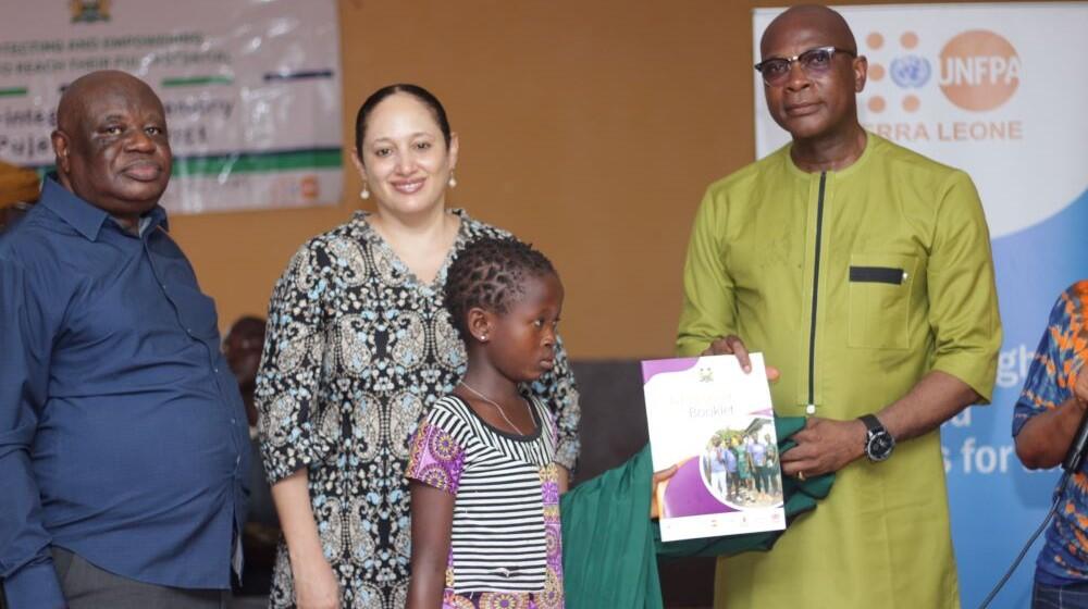 Conrad Sackey, Minister of Basic Education, and Nadia Rasheed of UNFPA, hand out school supplies during a ceremony honoring the reintegration of vulnerable girls into education. Photo Credit: UNFPA Sierra Leone/Islander Kabia